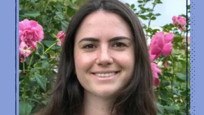 A smiling woman outdoors with pink flowers behind her.