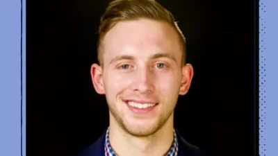 A headshot of a smiling man on a black background.