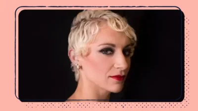 A headshot of a woman with short blonde hair on a black background.